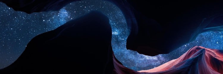 A view of a canyon illuminated by starlit sky, showcasing vibrant rock formations against a cosmic backdrop.