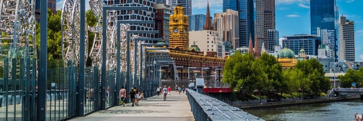 A vibrant cityscape of Melbourne featuring modern skyscrapers and historical buildings, viewed from a scenic waterfront walkway.